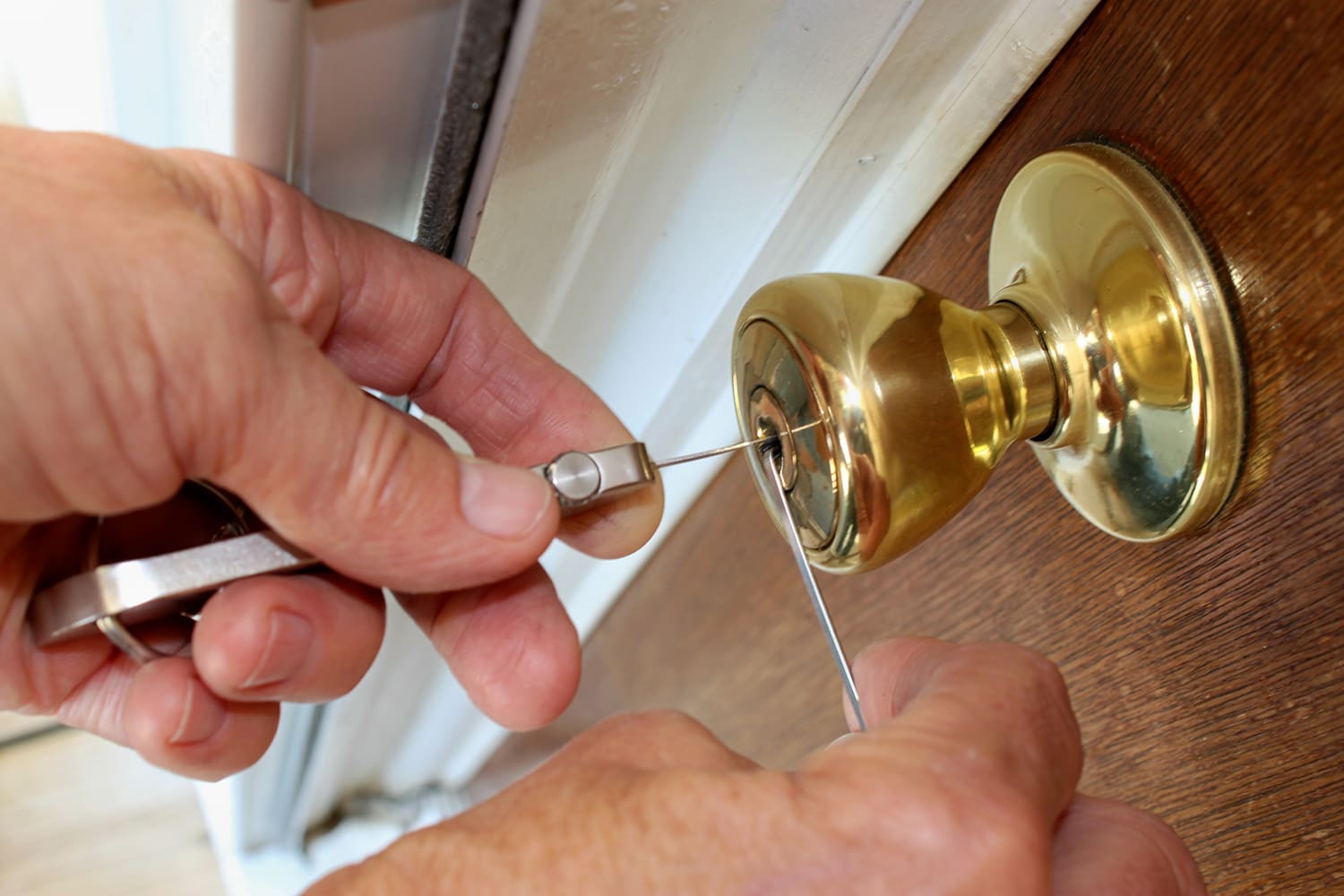 A closeup of a person using two tools to pick a lock on a door.